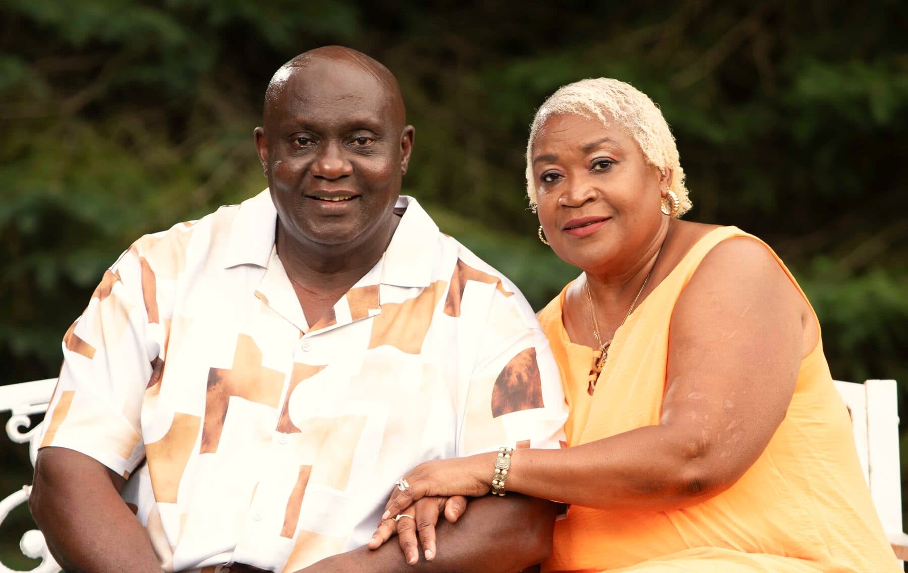 The property owners, Dymond's parents, seated together on a white garden bench at Rustic Hideaways