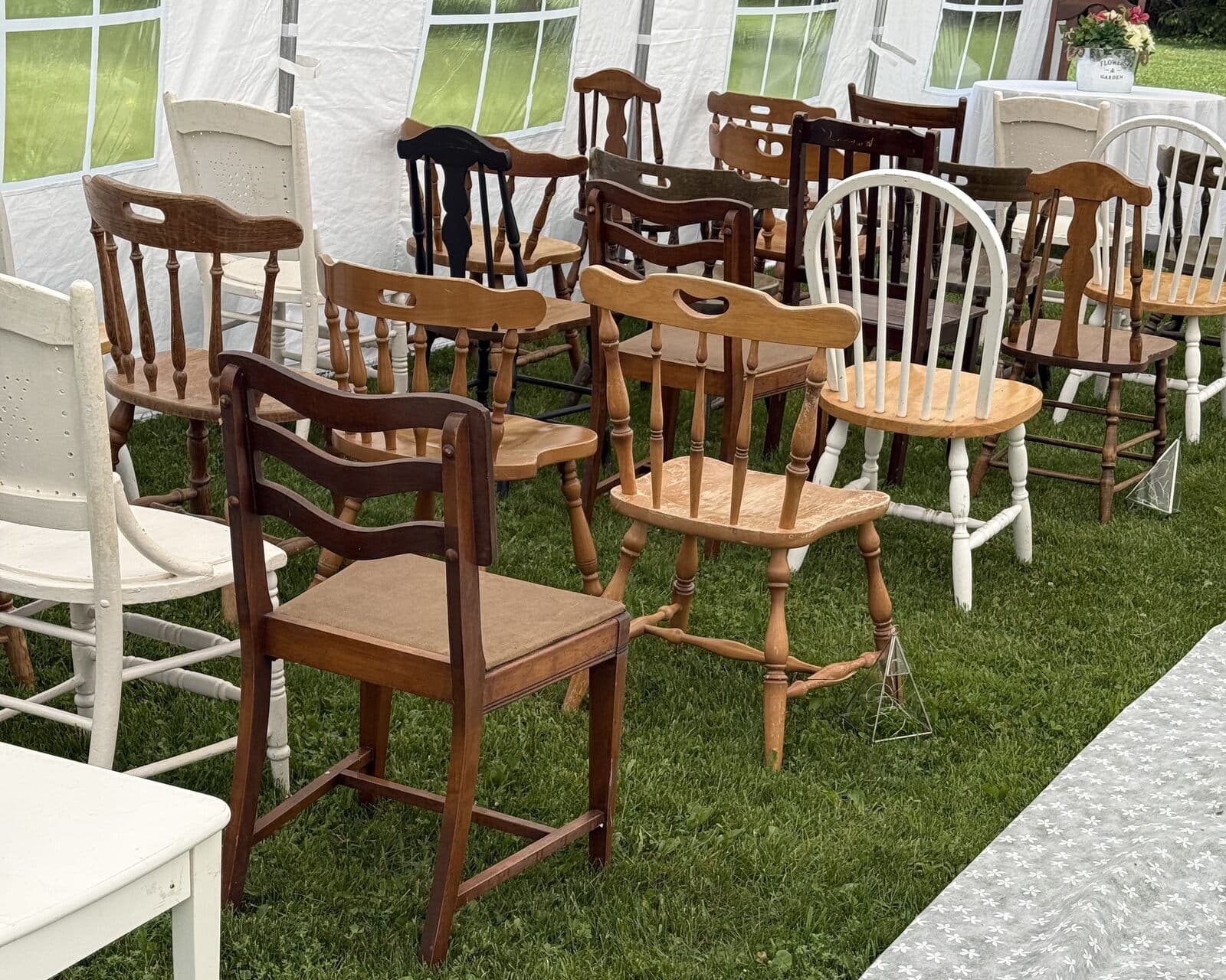 Rows of mismatched wooden and white chairs along a lace aisle runner on the lawn
